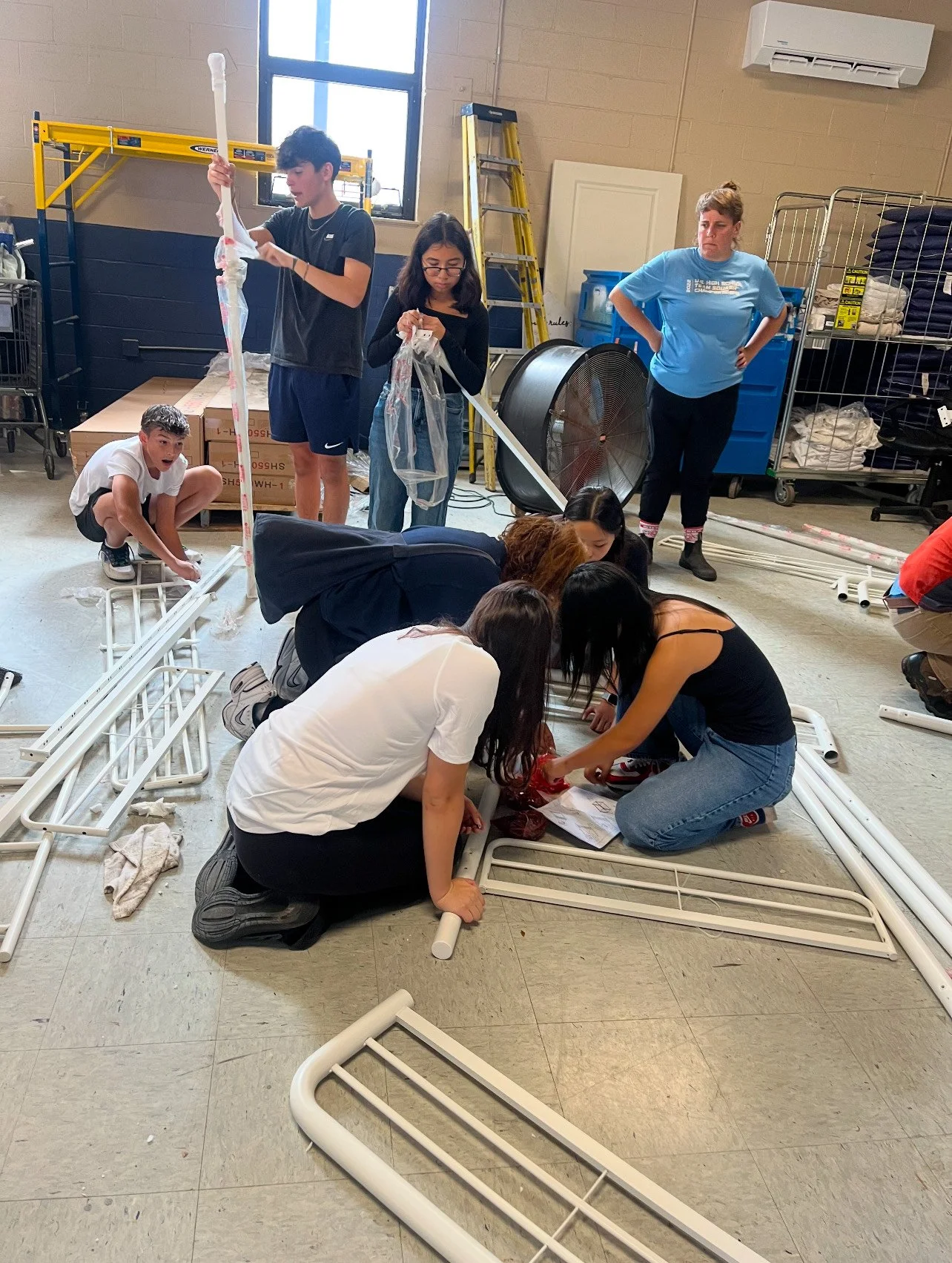 Volunteers kneeling on the floor putting together metal bed frames
